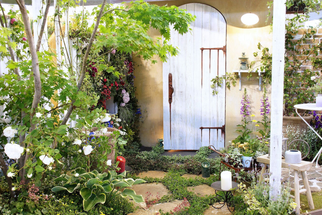 白い木製ドアと花や植栽に囲まれたナチュラルガーデンのアプローチ